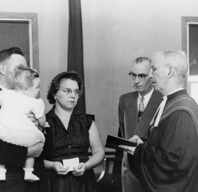 Rev. Dr. Joyce assisted by W.J. "Monty" Montgomery prepare to baptize this unidentifed child at Oxford United Church in Winnipeg, March 1956. UCCArchivesWpg oxford29